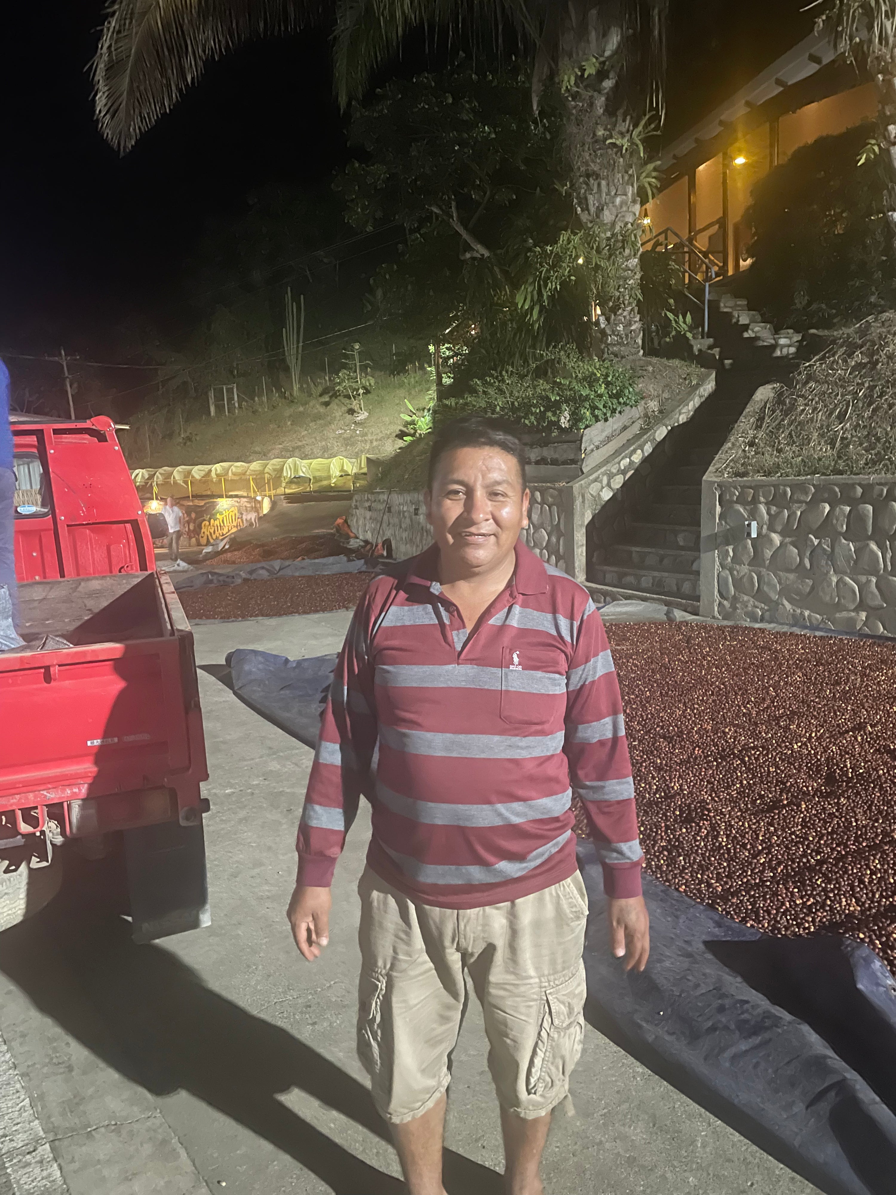 Man standing in front of a red truck at night with trees and steps in the background.